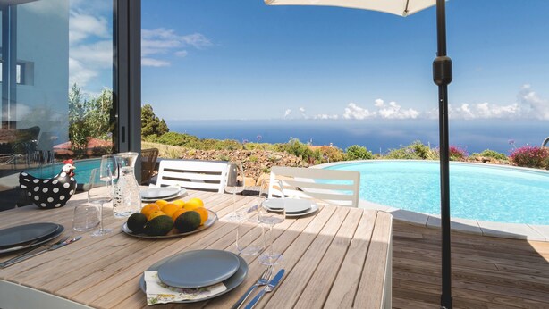 Ein Esstisch ist gedeckt mit Tellern, Besteck und Gläsern, mit Blick auf einen Pool und den Ozean.