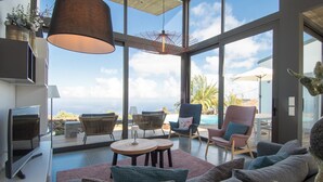 Ein modernes Wohnzimmer mit großer Glasswand, Pool und Außenmöbeln.