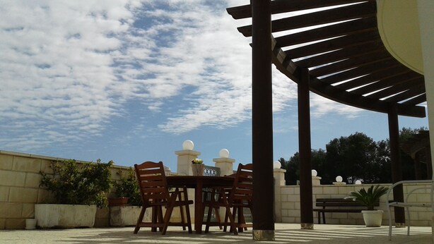 Una terrazza esterna con una pergola, un tavolo con sedie e piante in vaso.