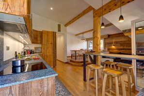 A modern kitchen with wooden accents, a central island, bar stools, and a dining area with a view.