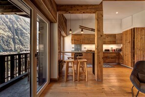 A modern kitchen with wooden cabinetry, a dining area with stools, and a view of a mountainous landscape through large sliding glass doors.