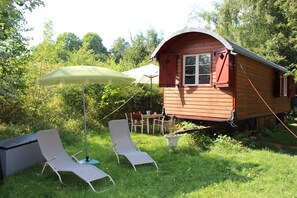 A wooden cabin with a red roof, a dining table with chairs, and two lounge chairs under a green umbrella. - "Sleeping Beauty" idyllically situated pack wagon, accommodation close to nature in the Westerwald (Hundsdorf)