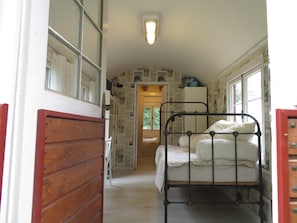A narrow hallway leading to a bedroom with a single bed, a wooden wardrobe, and a window with a view of greenery. - "Sleeping Beauty" idyllically situated pack wagon, accommodation close to nature in the Westerwald (Hundsdorf)