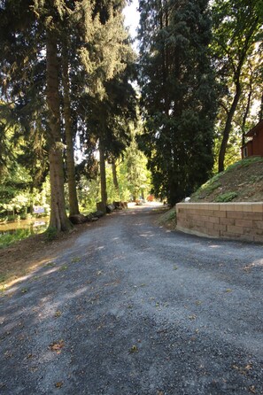 A gravel path in a wooded area with trees and a brick wall on the right. - "Sleeping Beauty" idyllically situated pack wagon, accommodation close to nature in the Westerwald (Hundsdorf)