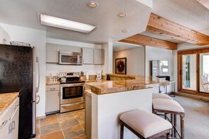 A modern kitchen with stainless steel appliances, a marble countertop, and wooden beams on the ceiling.