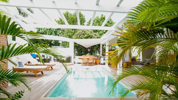 Un espace piscine doté d’une terrasse en bois, de chaises longues et d’une structure en forme de pergola.