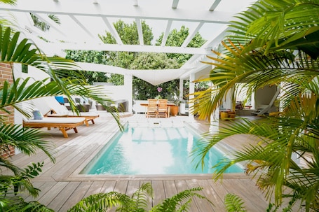 A pool area with wooden decking, lounge chairs, and a pergola structure.