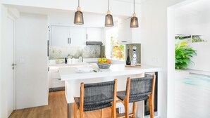 Une cuisine moderne avec des meubles blancs, un îlot central doté de sièges et des luminaires suspendus.