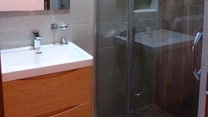Un bagno moderno con doccia vetro, mobile bagno in legno e un grande specchio sopra il lavandino.
