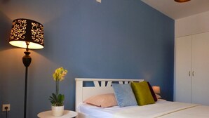 Una camera da letto con un letto bianco, un tavolino rotondo e una pianta in vaso, e una lampada da terra.
