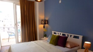 Una camera da letto con un letto, un comodino con una lampada, una sedia e vista sull'esterno.