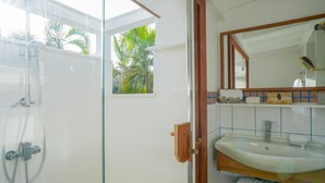 Un baño con ducha envuelta en vidrio, un lavabo blanco y un mueble de tocador de madera.