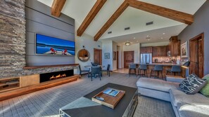 A spacious living room with a fireplace, a large TV mounted on a stone wall, and a cozy seating area.