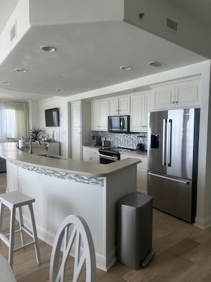 A modern kitchen with white cabinetry, a stainless steel refrigerator, a microwave, and a tiled backsplash.