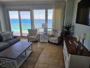A living room with a sofa, armchairs, a coffee table, a side table, and a view of the ocean through large windows.