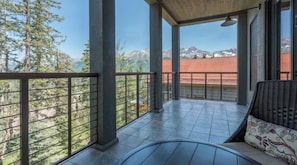 A balcony with a view of mountains, a wicker sofa, and a tiled floor.