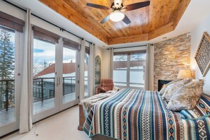 A bedroom with a large bed, a ceiling fan, and a view of a snowy landscape through large sliding doors. - Cassidy Ridge C-402 Mountain Village Condo (Mountain Village)