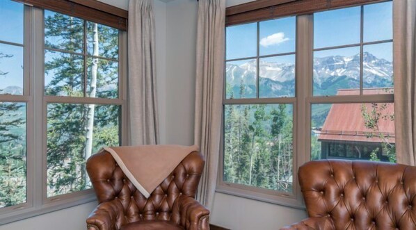 A room with two brown leather chairs, a window with a mountain view, and a curtain. - Cassidy Ridge C-402 Mountain Village Condo (Mountain Village)