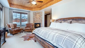 Un dormitorio con una cama grande, techo de madera, chimenea, sillones de cuero y pared de piedra.