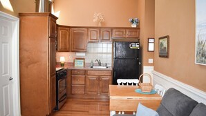 A compact kitchen with wooden cabinets, a black refrigerator, and a dining area with a gray sofa and a small table.