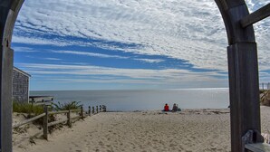 A beach scene with a wooden archway, a sandy beach, and a calm sea. - End Unit Condo with breathtaking ocean views! (Dennis Port)