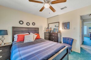 A bedroom with a bed, dresser, chair, and ceiling fan.