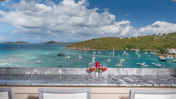 Een balkon met uitzicht op een turquoise zee, boten en een groene heuvel.