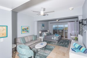 Une chambre d’hôtel moderne, dotée d’un lit, d’un canapé et d’un fauteuil, ainsi que d’un balcon avec des rideaux et d’œuvres d’art accrochées aux murs.