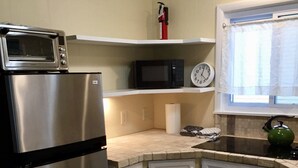Una cocina con un refrigerador de acero inoxidable, un microondas, un reloj y una ventana con cortina.