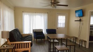 Una habitación con ventilador de techo, televisión montada en la pared, una mesa de comedor con sillas y un sofá.