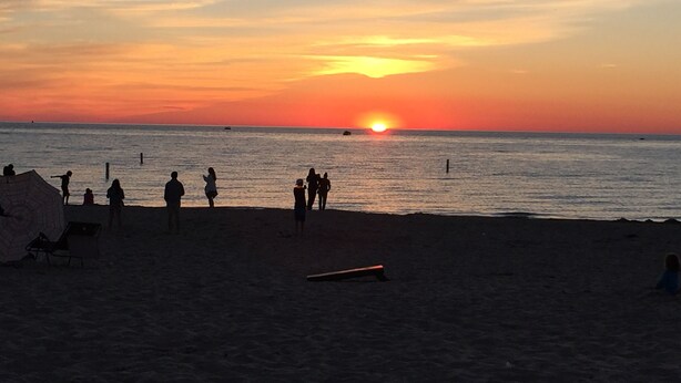 Escena de playa con gente y un atardecer.