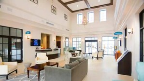 Eine großzügige Lobby mit grauem Sofa, Couchtisch und Wand-Fernseher. Schilder weisen den Weg zum Restaurant und zur Lobby.