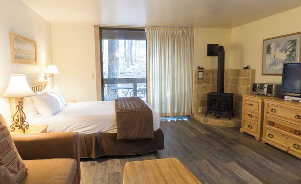 Ein Hotelzimmer mit Bett, Sofa, Fernseher, Kamin und einem Fenster mit Vorhängen.