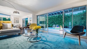 Una sala de estar moderna con sofá, mesa de centro y sillones, ventanas amplias y vista a un jardín.