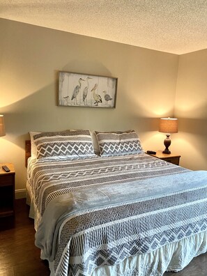 A bedroom with a bed, two nightstands, a lamp, and a wall-mounted painting.