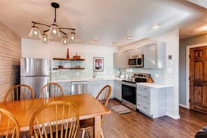 A modern kitchen with white cabinets, stainless steel appliances, and a wooden dining table.