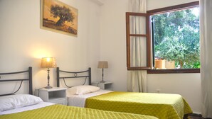 Une chambre avec deux lits, une fenêtre donnant sur des arbres et un tableau accroché au mur.