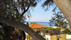 Un bâtiment situé sur la côte, avec un toit recouvert de tuiles rouges, un escalier menant à un balcon et une vue sur la mer.