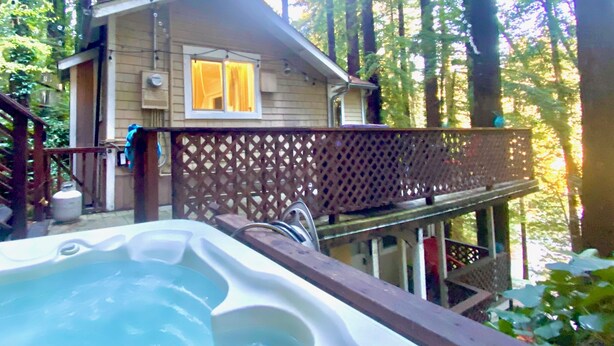 A cabin with a hot tub, wooden deck, and a view of the forest.