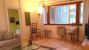 A living room with a glass coffee table, a sofa, two wooden chairs, a small side table, and a radiator.