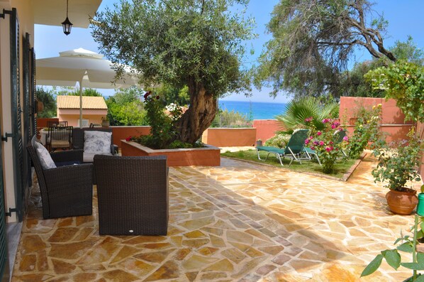 A patio with stone flooring, wicker furniture, and potted plants. - Beach houses in Corfu “Angelos” at Agios Gordios (Agios Gordios)