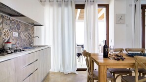 A kitchen with a modern stove, a dining area with a wooden table and chairs, and a view of the outdoors through a window.