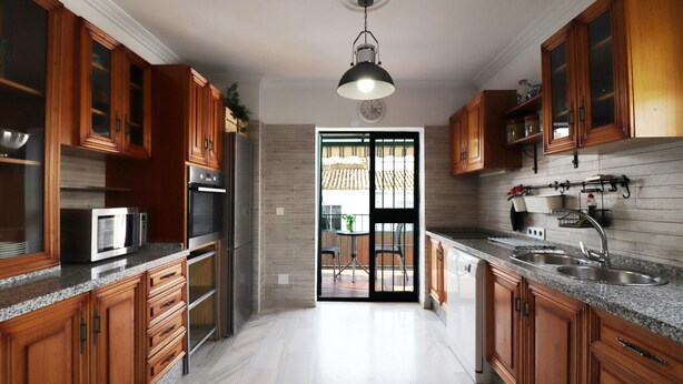 A modern kitchen with wooden cabinets, granite countertops, stainless steel appliances, and a black pendant light. - 1028 Casa Evelyn D (Nerja)