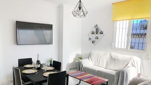 A modern living room with a dining area, a sofa, a TV, and a window with bars. - 1028 Casa Evelyn D (Nerja)