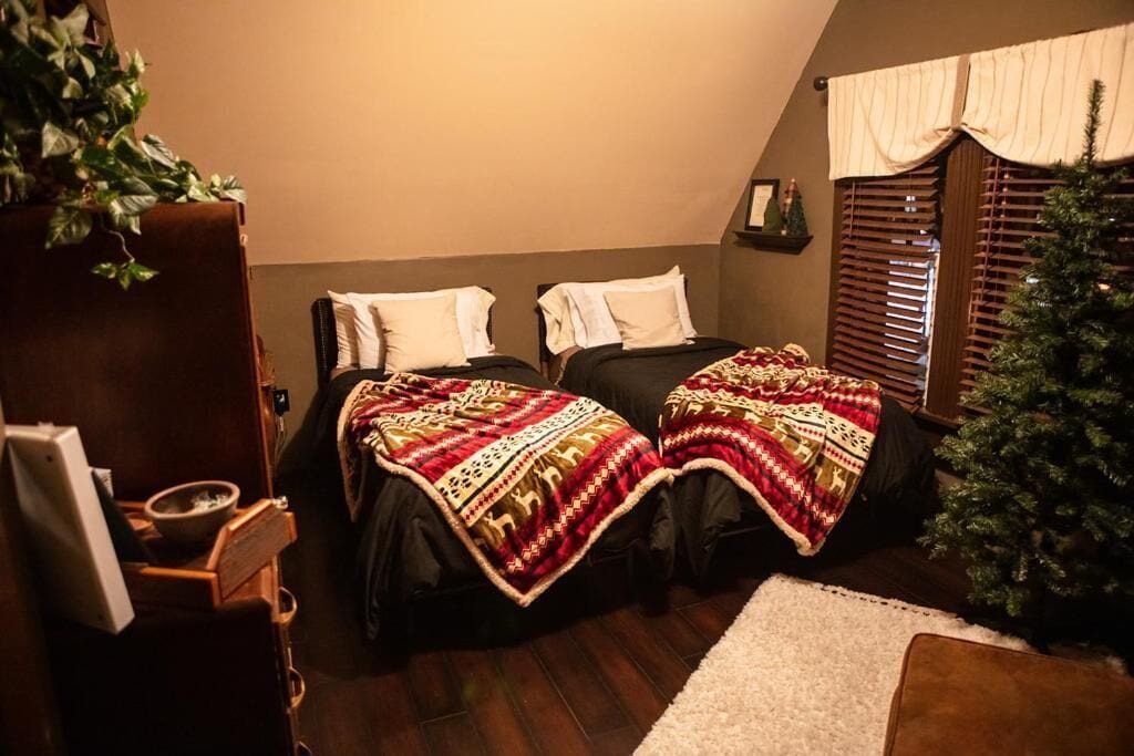 A cozy room with two beds, a small Christmas tree, and a wooden cabinet.