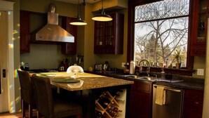 A kitchen with a large island, wine rack, and a window with a view of trees. - The Katherine Holle House (Watertown)