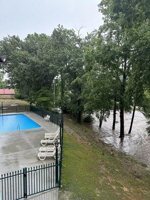 A swimming pool with a fenced deck, surrounded by trees and a flooded area.