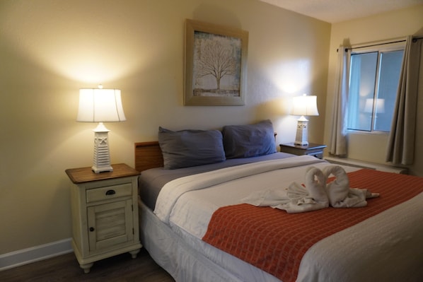 A hotel room with a bed, two bedside lamps, a nightstand, a framed picture on the wall, and a window with curtains.