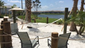 A beachside area with a hammock, two lounge chairs, and a view of a body of water and distant mountains. - Modern 7BR w/Pool/ Minutes from Disney/ ESPN (Kissimmee)