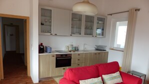 Un ambiente compatto con angolo cottura, caratterizzato da mobili, un tavolo da pranzo e un divano rosso con cuscini decorativi.